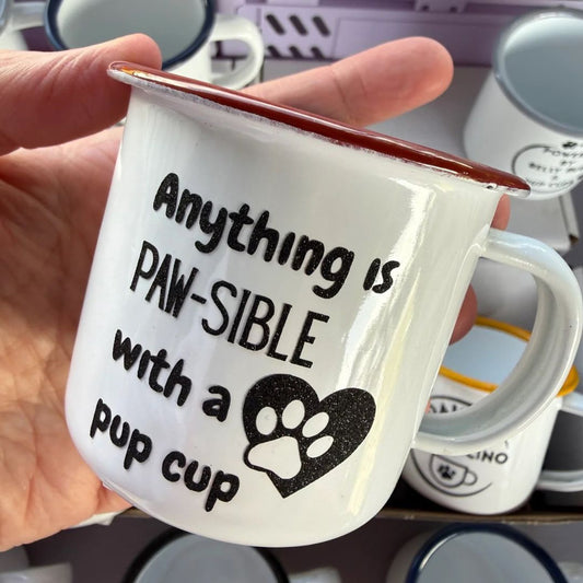 White mug with red rim and black text held by a hand, with more mugs in the background.