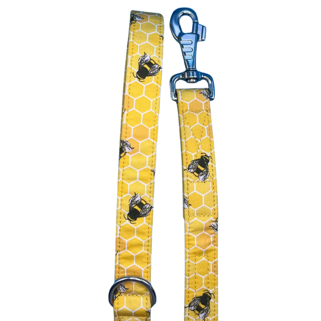 A yellow dog lead with a honeycomb pattern and bees, featuring silver metal hardware and a blue swivel clip.