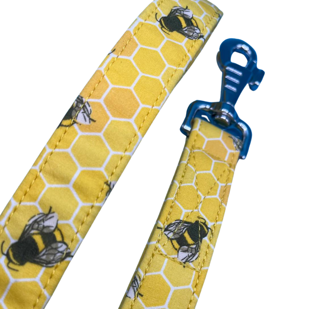 A close up of a yellow dog lead with a honeycomb pattern and bees, featuring silver metal hardware and a blue swivel clip.