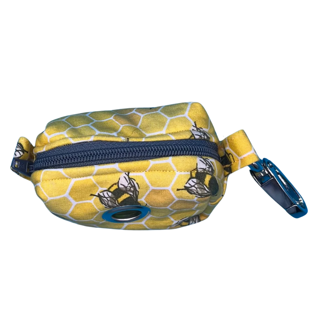 A top view of a fabric bee hive poo bag holder with a yellow honeycomb pattern and black bees, featuring a white zip and metal accessories.