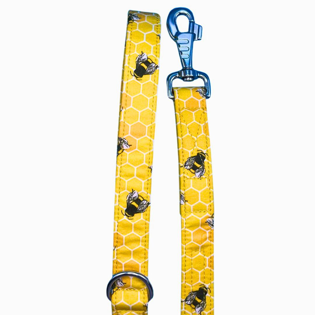 A yellow dog lead with a honeycomb pattern and bees, featuring silver metal hardware and a blue swivel clip.