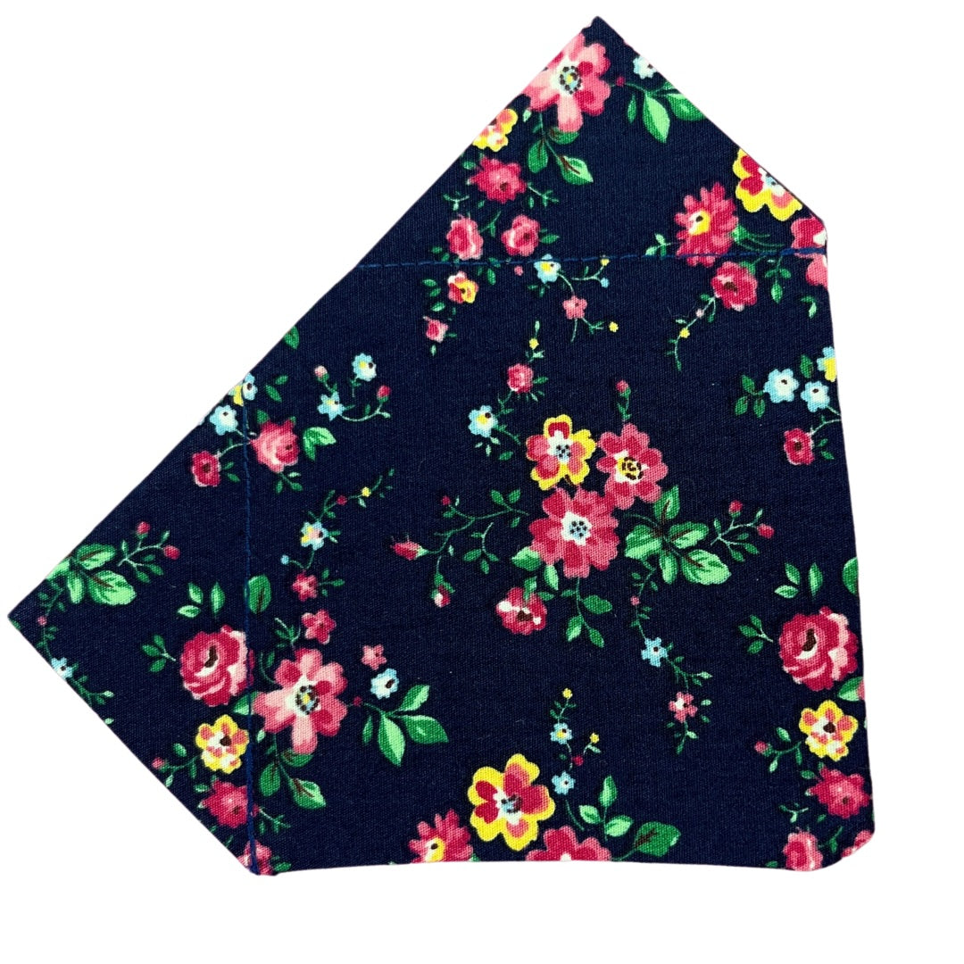 A navy cotton dog bandana with a floral pattern consisting of pink, yellow, and green flowers.