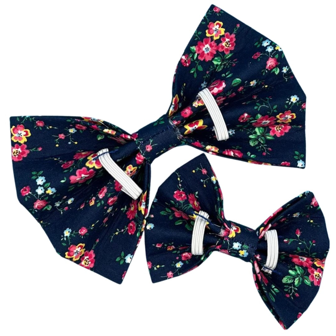 The back of a navy blue dog bow with a floral pattern, featuring pink and green flowers.