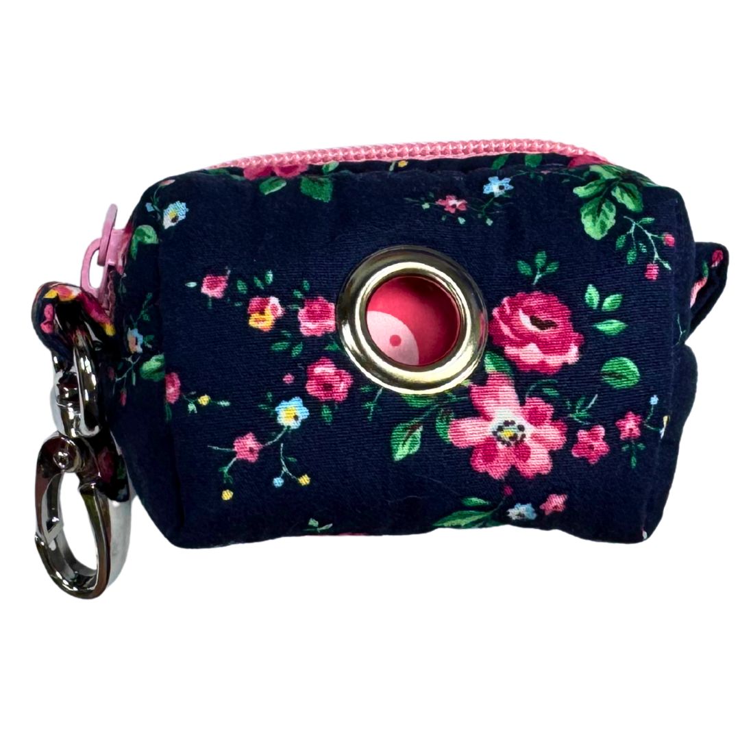 A fabric poo bag holder with a floral pattern, featuring a metal accessory and a colour pink zip.