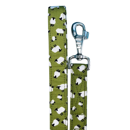 A green fabric dog lead with a white sheep pattern and a metal swivel clip and D ring.