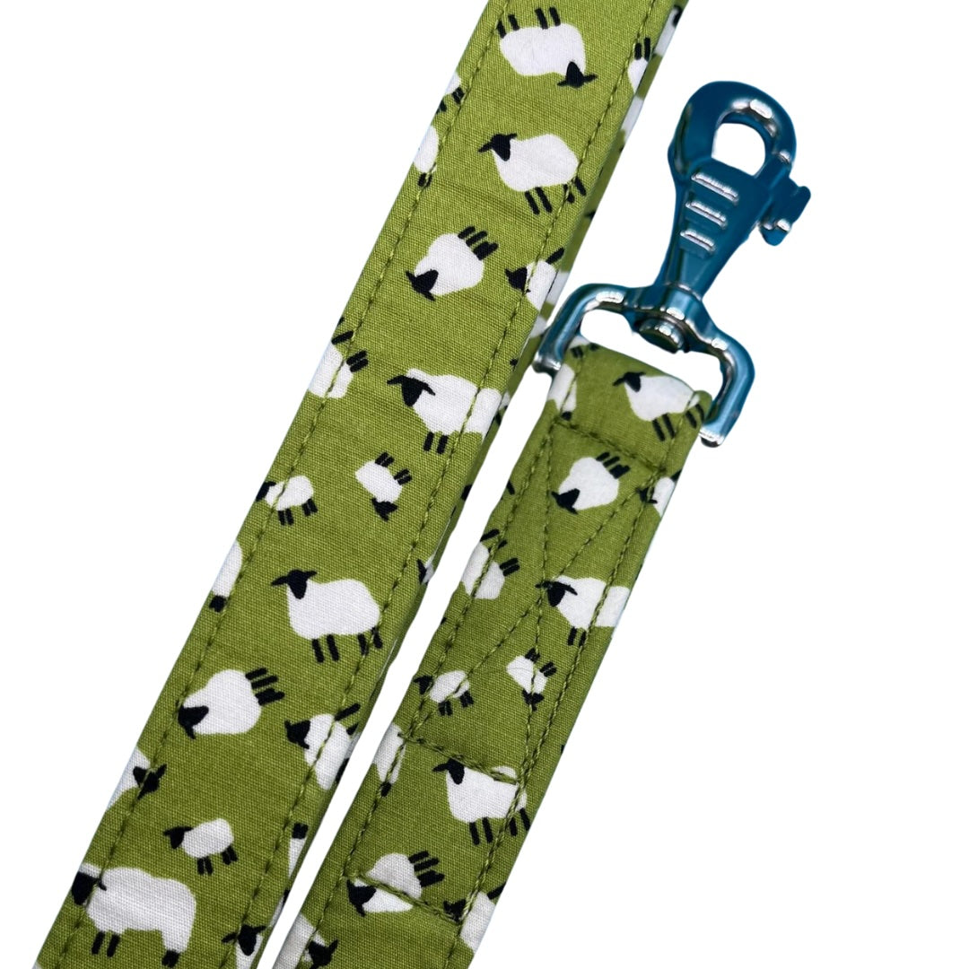 A green fabric dog lead with a white sheep pattern and a metal swivel clip and D ring.