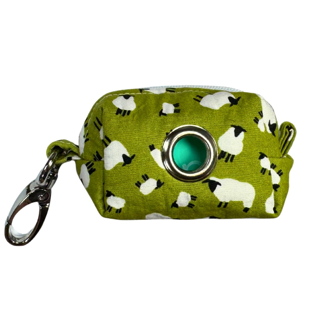 A fabric poo bag holder with a green background and white sheep patterns, featuring a metal keychain.