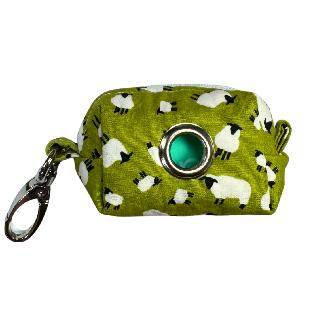 A fabric poo bag holder with a green background and white sheep patterns, featuring a metal keychain.