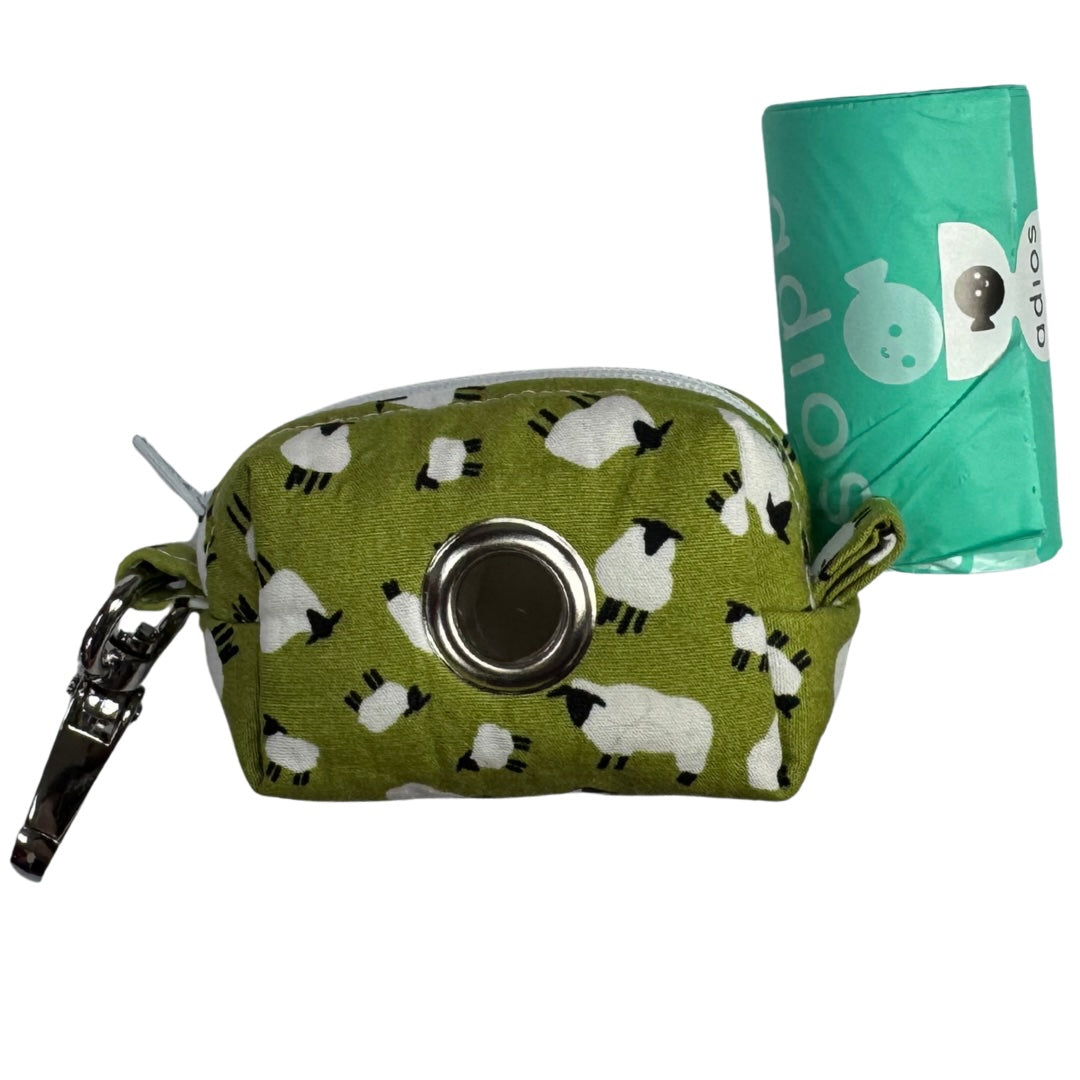 A fabric poo bag holder with a green background and white sheep pattern, with a roll of adios poo bags.