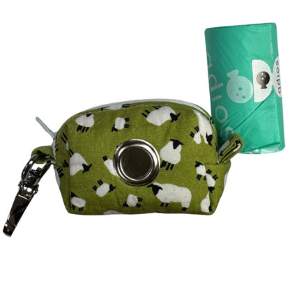 A fabric poo bag holder with a green background and white sheep pattern, with a roll of adios poo bags.