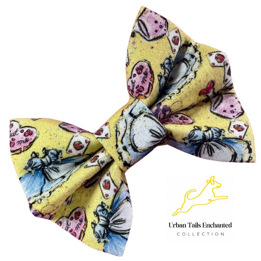 A yellow cotton dog bow tie with an Alice in wonderland pattern, including the eat me biscuit, p[laying cards, and Alice's blue dress