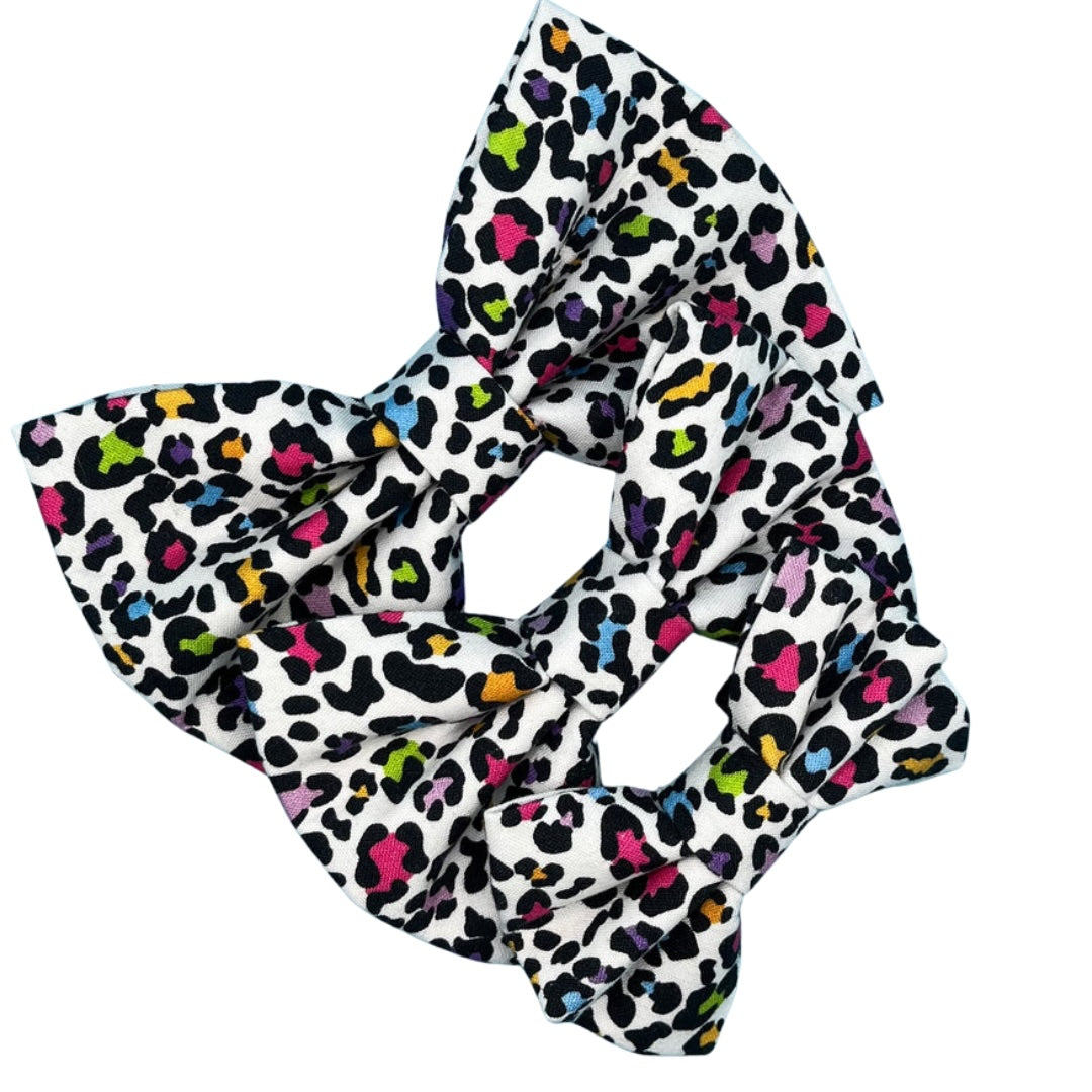 A multicoloured leopard print dog bow tie with a white background in three sizes, small, medium and large.