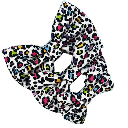 A multicoloured leopard print dog bow tie with a white background in three sizes, small, medium and large.