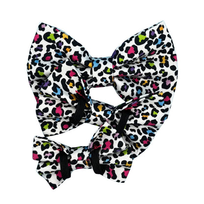 A multicoloured leopard print dog bow tie with a white background in three sizes, small, medium and large showing the double elastic.