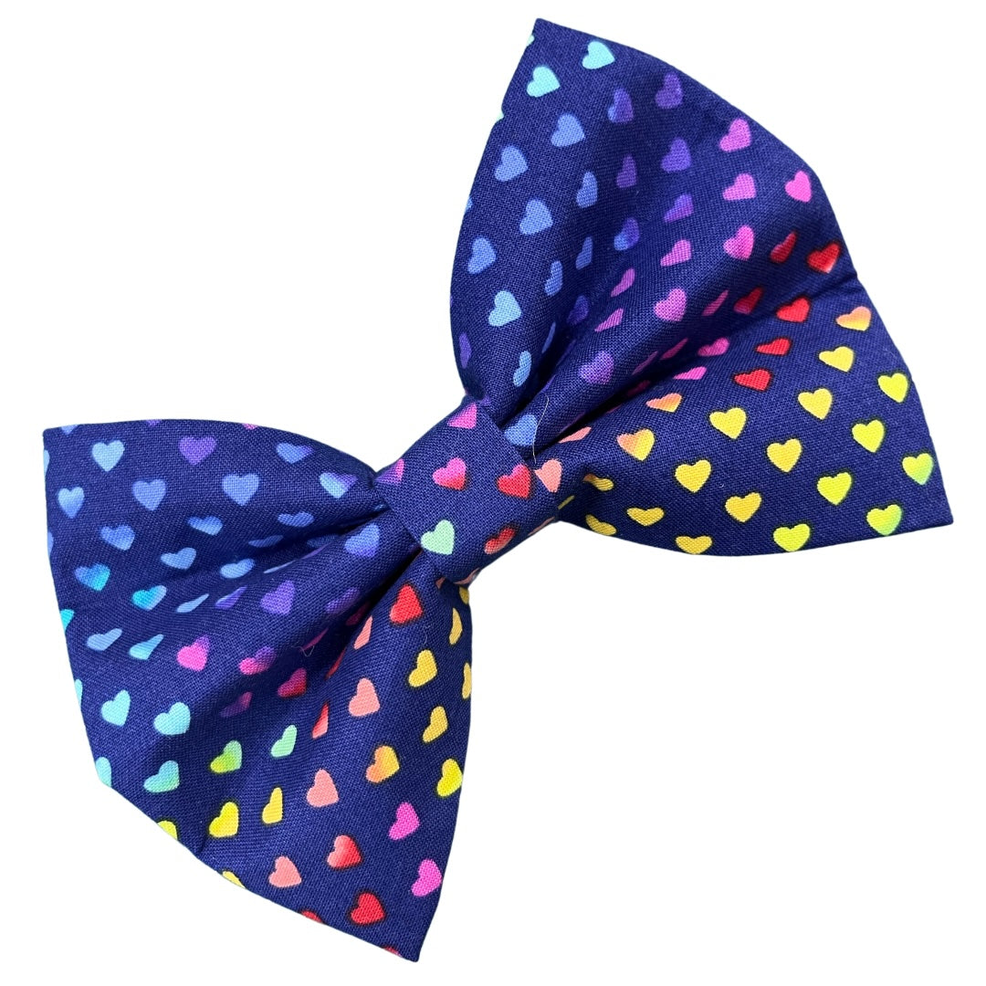 A blue dog bow tie with multicolored heart polka dots.