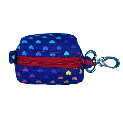 A top view of a fabric poo bag holder with a heart polka dot pattern and a metal accessory, finished with a contrasting red zip.