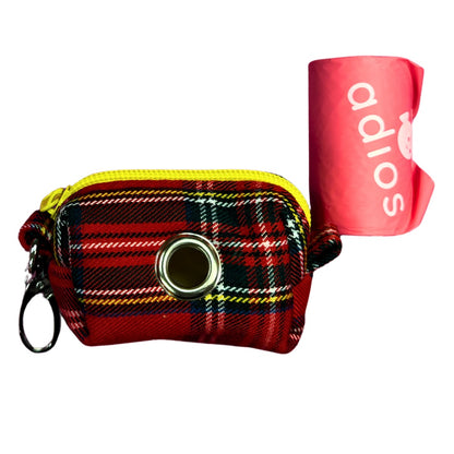 Plaid red poo bag holder with yellow zipper and circular metal clasp next to a roll of poo bag holders