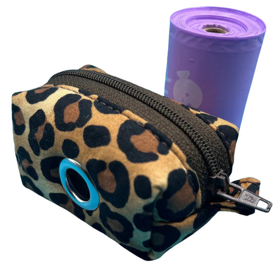 A fabric poo bag holder in brown and black animal print, featuring a roll of purple poo bags, with metal accessories and a colour contrasting zip.