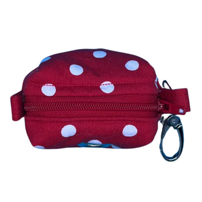 A top view of a red fabric poo bag holder with white polka dots, a red zip and a metal clip.