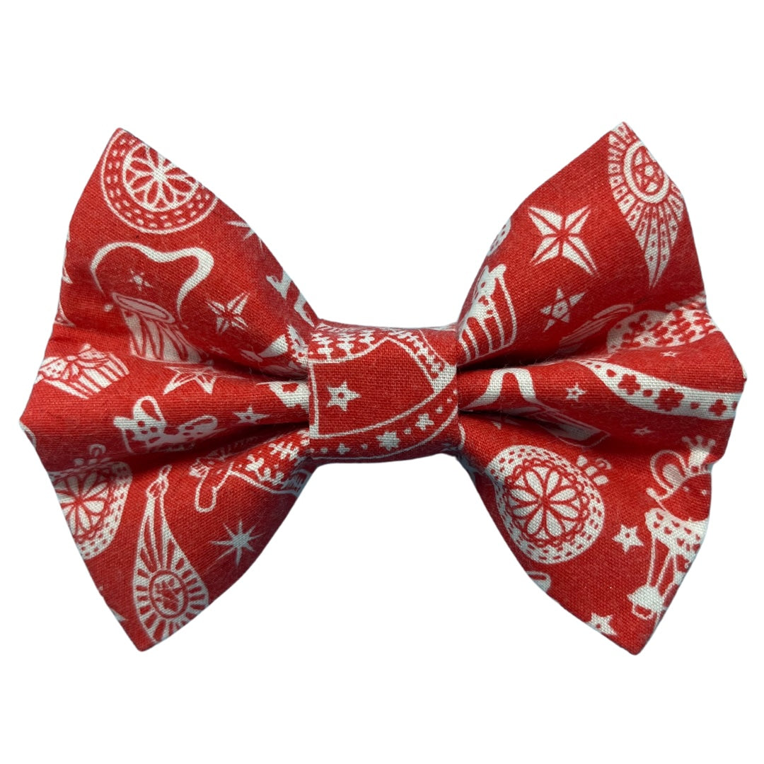 A red handmade dog bow tie with a Christmas-themed pattern that includes a rocking horse, baubles and a mouse