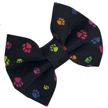 A fabric dog bow with a paw print pattern on a black background