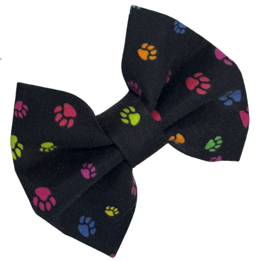 A fabric dog bow with a paw print pattern on a black background