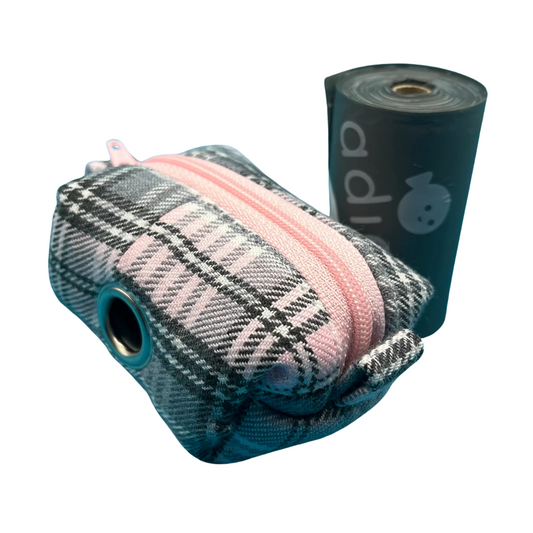 A baby pink and grey tartan patterned fabric poo bag holder with a pink zipper and metal accessories, alongside a roll of black poo bags.