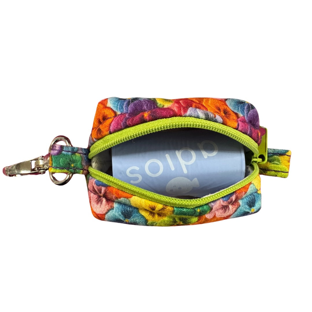 A colourful pansy floral fabric poo bag holder with metal accessories and a green zipper.