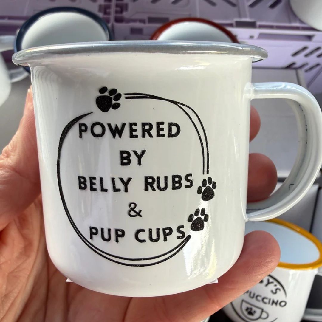 White mug with 'Powered by Belly Rubs & Pup Cups' text held in a hand.