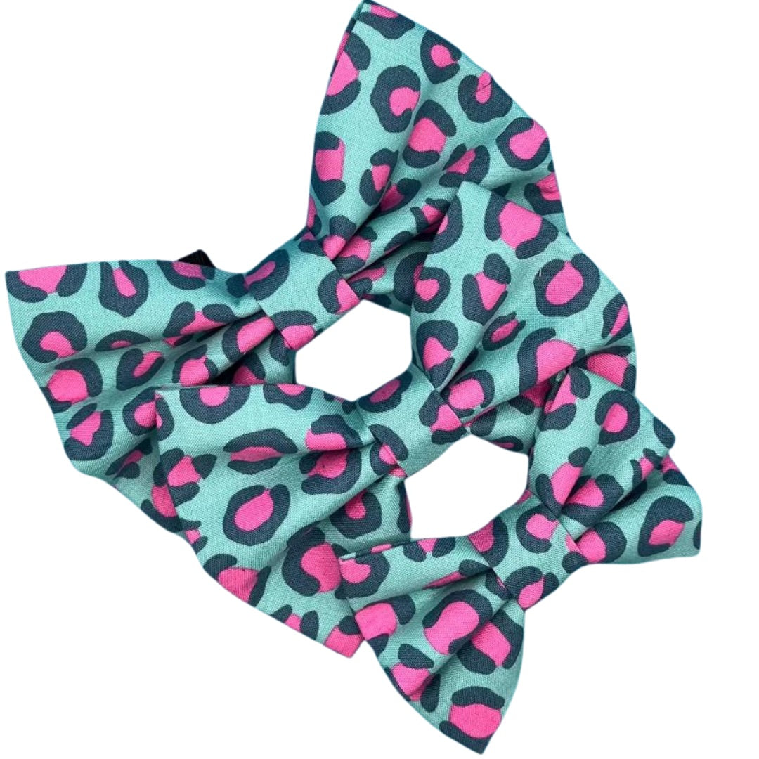 A fabric dog bow with a leopard print pattern in pink and teal designed to slip onto a collar.