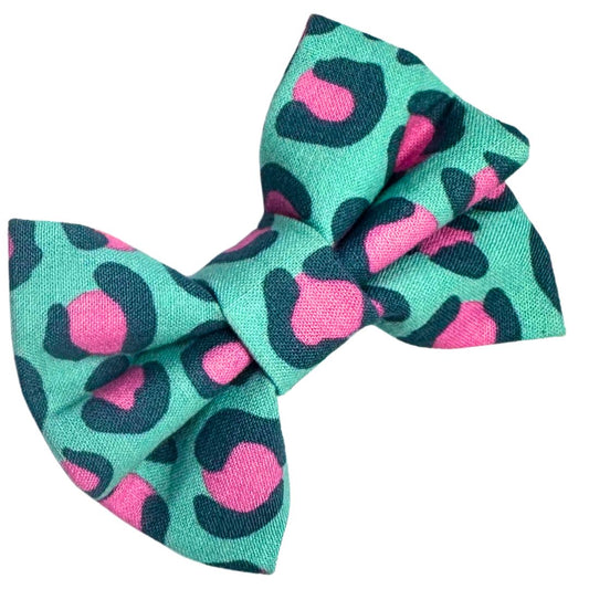 A fabric dog bow with a leopard print pattern in pink and teal designed to slip onto a collar.