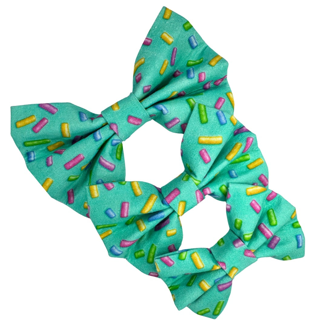Three green dog bow ties in small, medium and large with a multi-coloured sprinkle pattern on it.