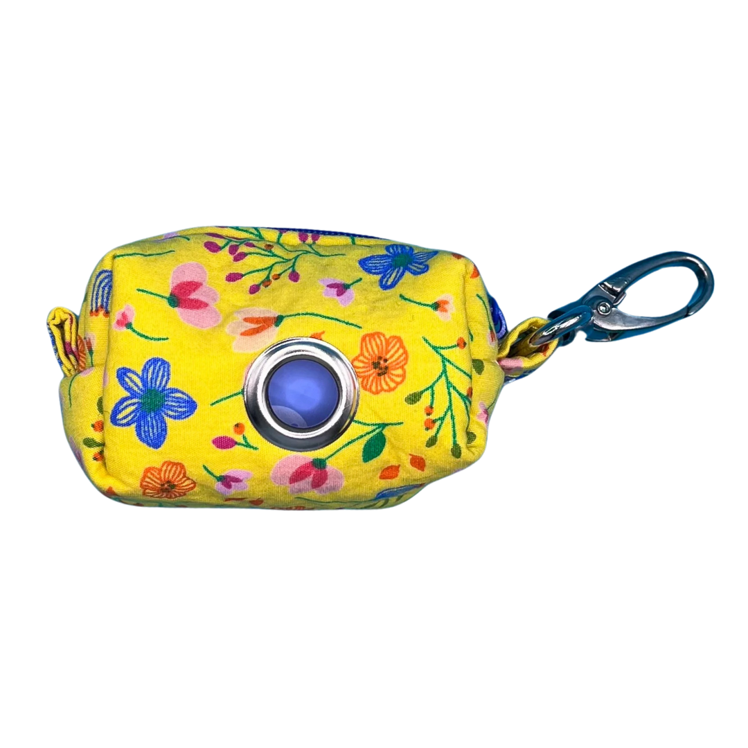 A yellow fabric poo bag holder with a floral pattern, featuring a metal clip and a contrasting blue zipper.