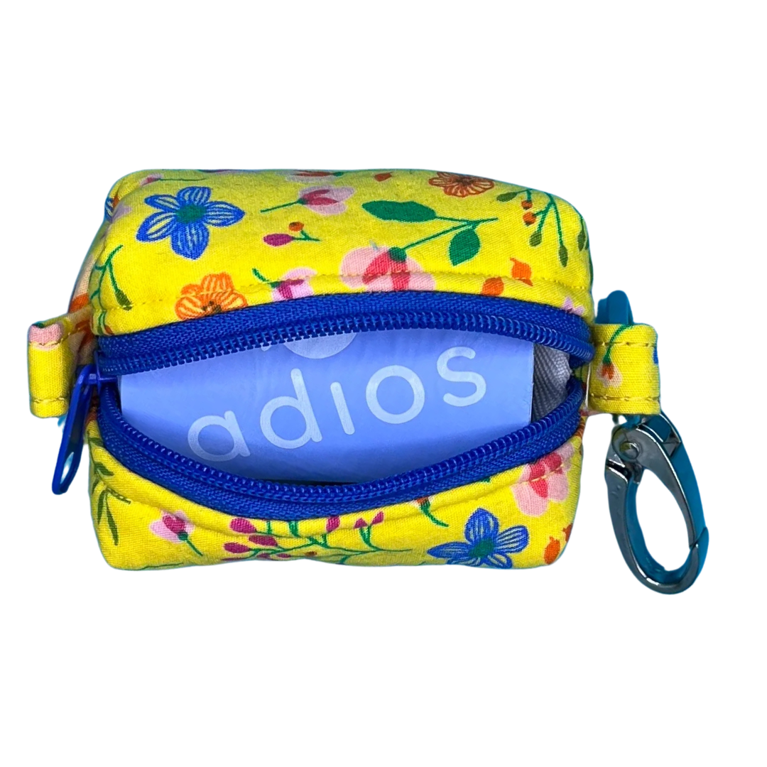 An open yellow fabric poo bag holder with a floral pattern, featuring a metal clip and a contrasting blue zipper.