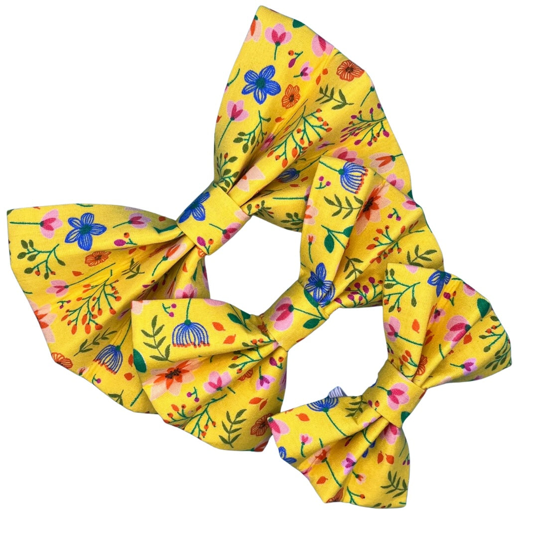 Three yellow dog bow ties with a floral pattern in pink and blue