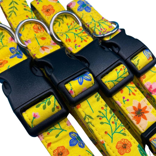 A close up of four yellow dog collars with a floral pattern, a silver metal D ring, plastic tri-glide adjustor, and a plastic clip